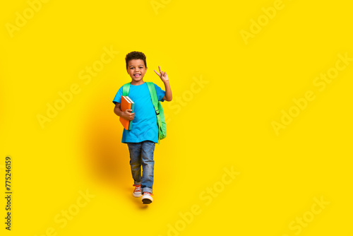 Full length photo of friendly cool preteen boy wear blue t-shirt walking showing v-sign empty space isolated yellow color background