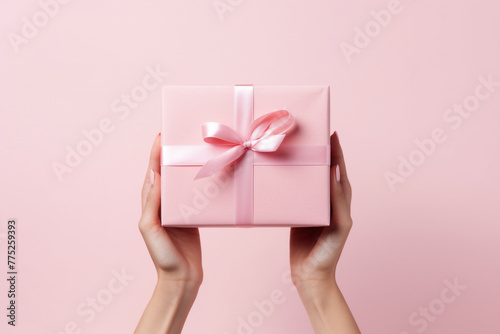 Minimal pink background with woman hands holding a wrapped gift box seen from a low angle for a birthday 