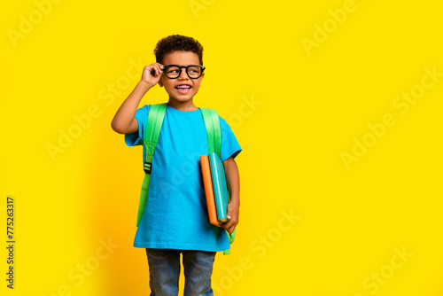 Photo of cheerful tricky preteen boy wear blue t-shirt spectacles holding book looking empty space isolated yellow color background