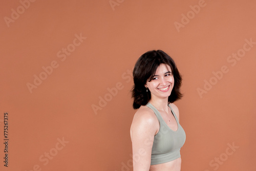Portrait of a smiling young woman in casual attire against a warm brown background.