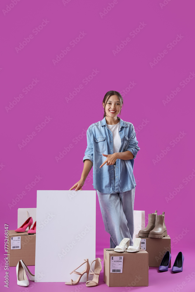 Young Asian seller with blank poster and shoes on purple background Young Asian seller with blank poster and shoes on purple background