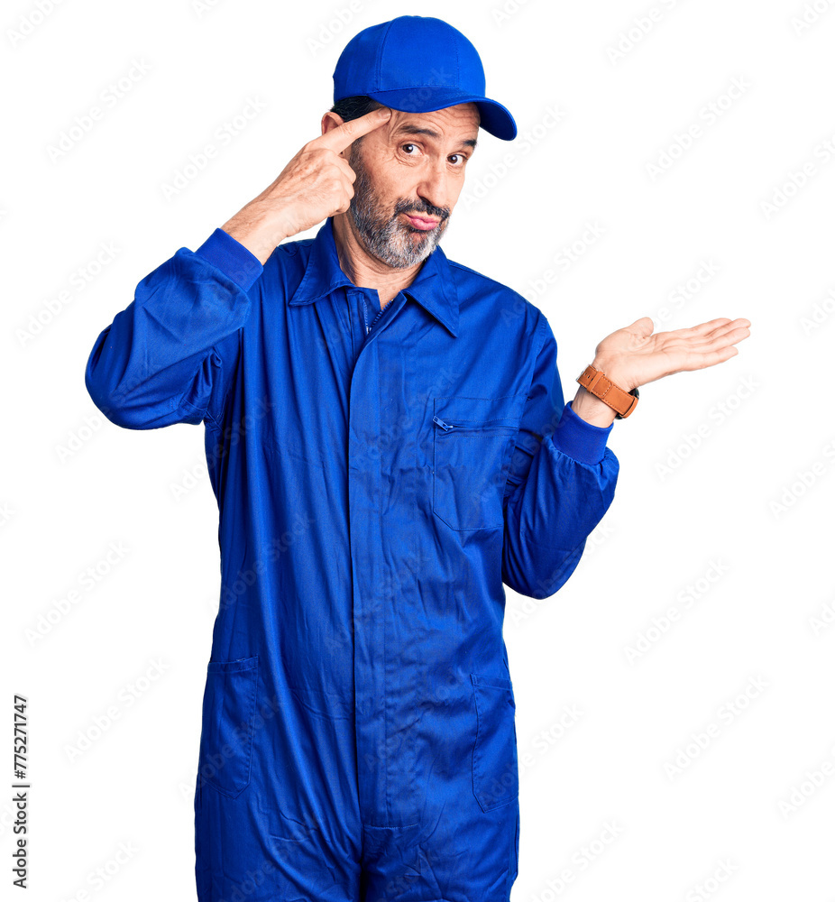 Middle age handsome man wearing mechanic uniform confused and annoyed with open palm showing copy space and pointing finger to forehead. think about it.