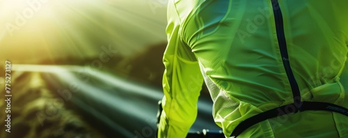 Cyclist viewed from behind on sunlit road. Close-up sports and fitness concept with vibrant green jacket. photo