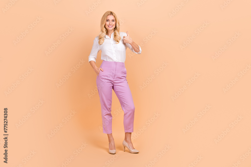 Full length photo of adorable confident woman wear white shirt showing thumb up empty space isolated beige color background Full length photo of adorable confident woman wear white shirt showing thumb up empty space isolated beige color background