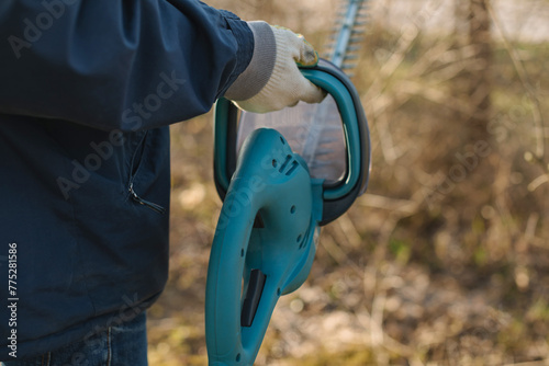 Close-up of a man holding an electric brush cutter to cut off the branches in the garden on a spring day.