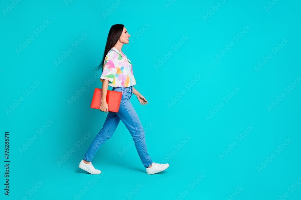Full size profile photo of pretty young woman hold netbook walk empty space wear shirt isolated on teal color background Full size profile photo of pretty young woman hold netbook walk empty space wear shirt isolated on teal color background