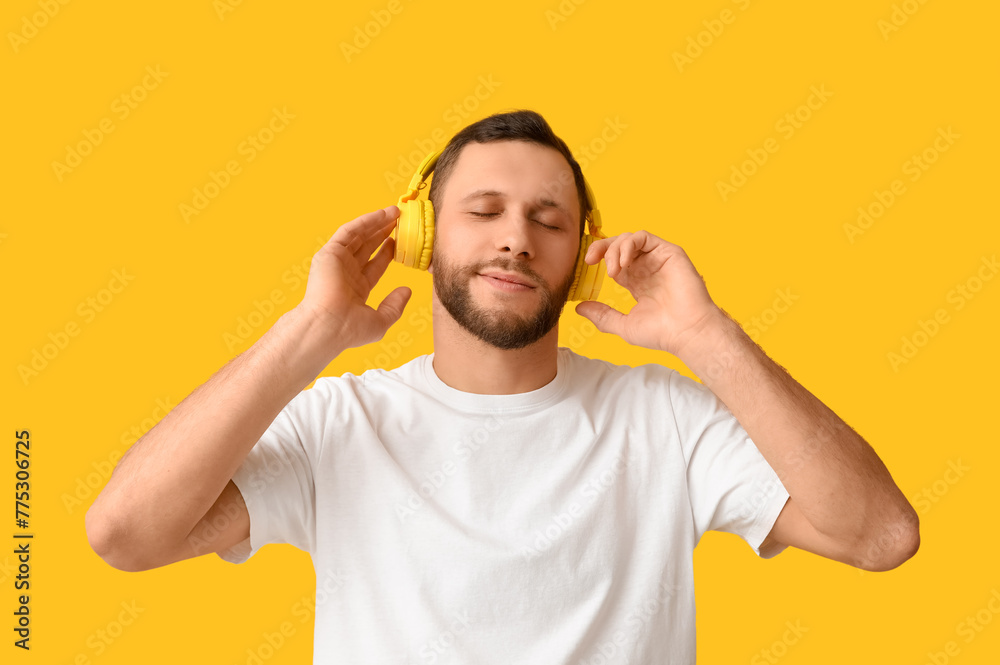 Young man in modern headphones on yellow background - obrazy, fototapety, plakaty 