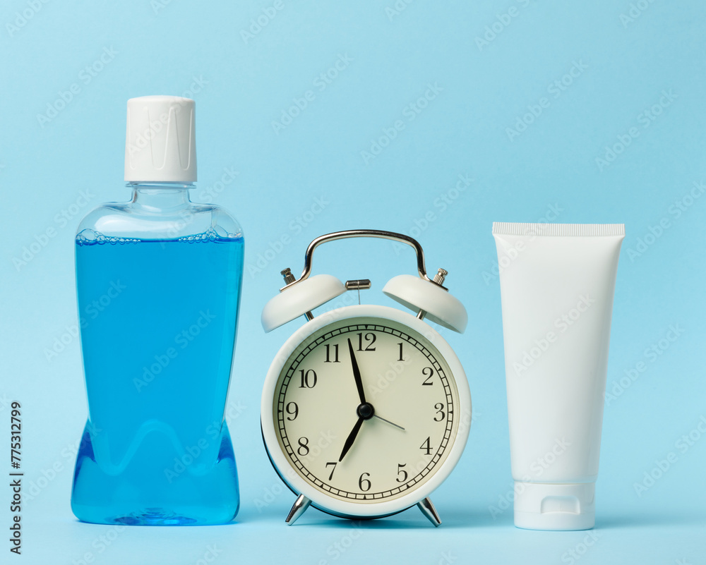 Plastic bottle with mouthwash, tube of toothpaste and round alarm clock ...