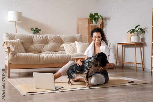 Sporty young African-American woman with cocker spaniel sitting after training at home