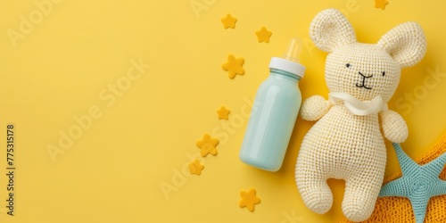 Cute baby product banner, knitted toy and baby bottle laying on tender yellow background with copy space. © JW Studio