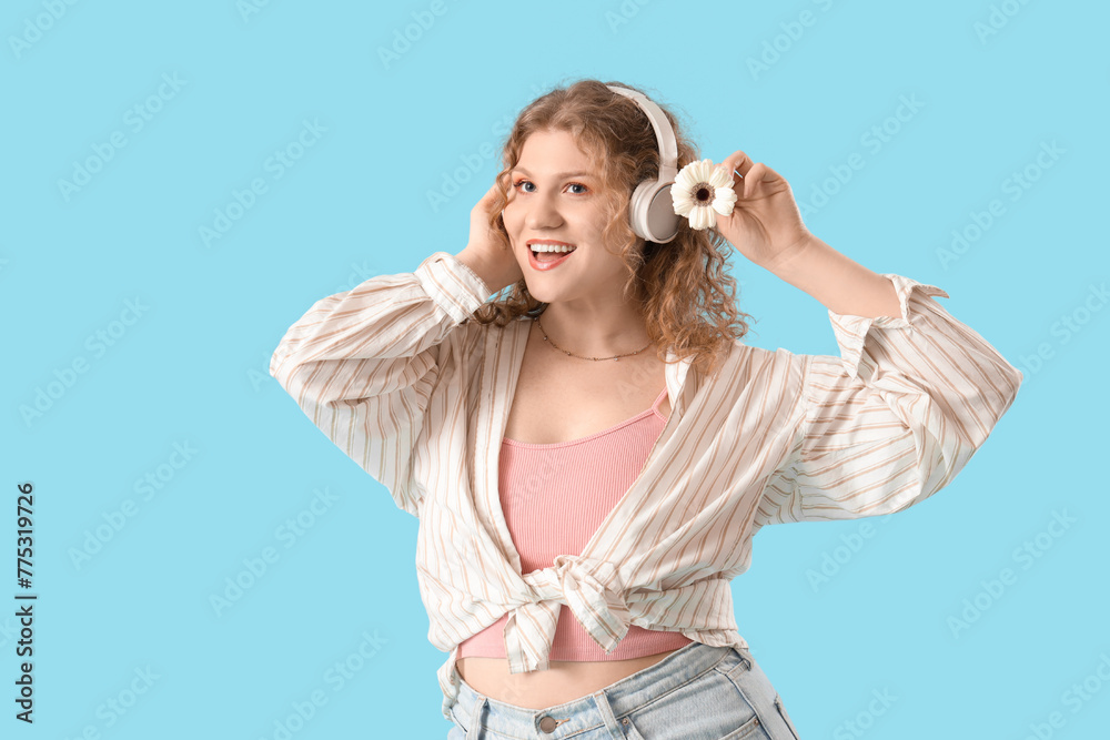 Pretty young woman in headphones with beautiful gerbera flower on blue background - obrazy, fototapety, plakaty 