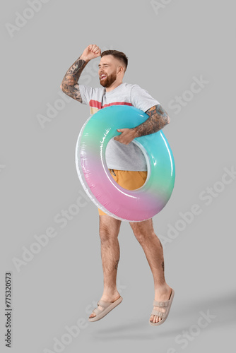 Young man with inflatable ring on grey background