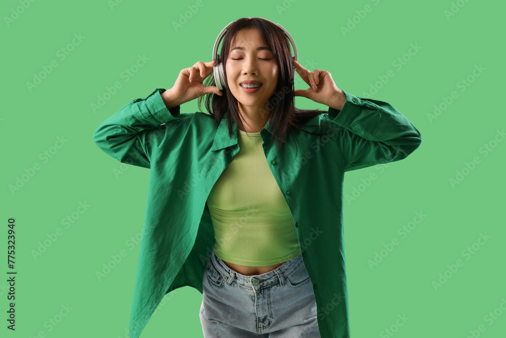 Naklejka premium Asian young woman listening music in headphones on green background