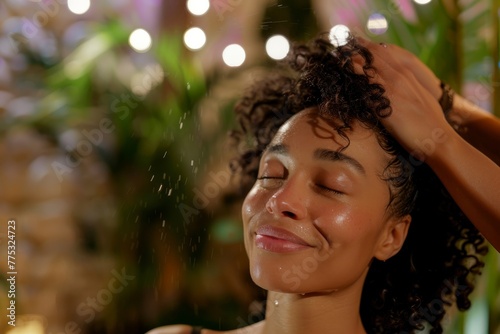 The image captures a woman with curly hair enjoying refreshing water spray with a smile and closed eyes