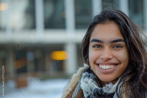 A young woman with a warm smile is wrapped up in winter wear, with cityscape behind © ChaoticMind
