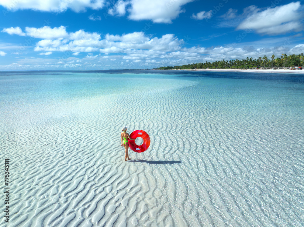 Aerial view of sporty slim woman with swimming ring, sandy beach, blue sea during low tide at sunny summer day in Zanzibar island. Top view of beautiful girl, sandbank, ocean, sky with clouds, palms Aerial view of sporty slim woman with swimming ring, sandy beach, blue sea during low tide at sunny summer day in Zanzibar island. Top view of beautiful girl, sandbank, ocean, sky with clouds, palms