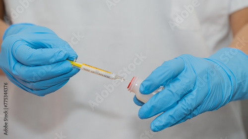 A person wearing blue gloves is holding a thermometer and a syringe