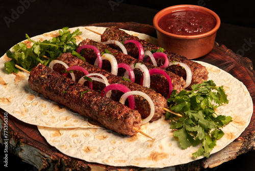 Kebab: grilled sausages on skewers of minced meat with pita bread and barbecue sauce decorated with pickled onions on a wooden board. Oriental cuisine