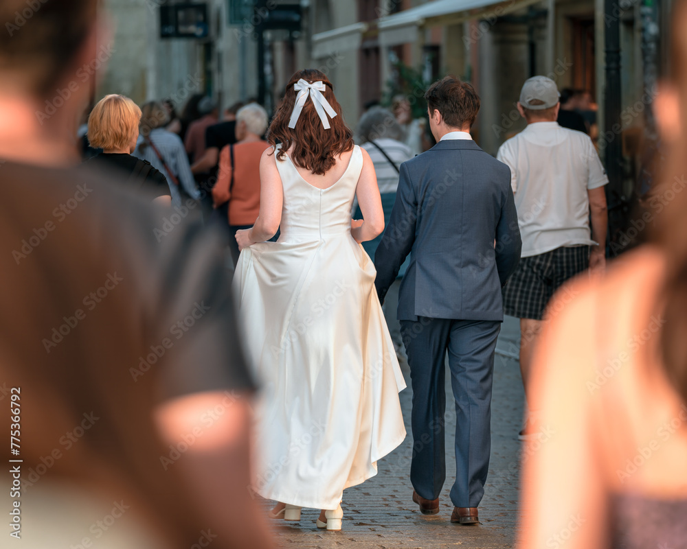 A young generation Z couple in wedding dresses walks among passers-by along a busy city street, symbolizing a new journey together against the backdrop of everyday city life