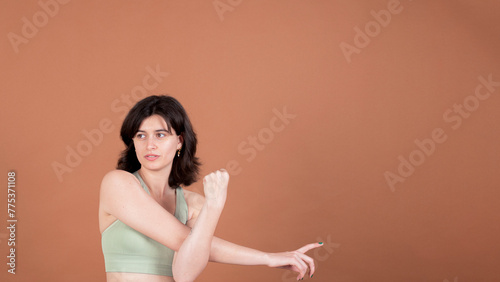 A portrait of a young girl stretching her arms while pointing her finger to one side of the composition, indicating direction or focus, against a neutral background.