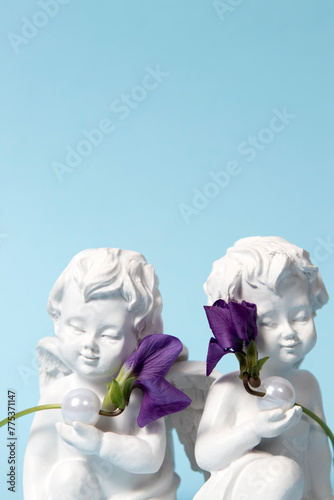 Fototapeta Naklejka Na Ścianę i Meble -  Angels holding white pearls and wild violet flowers on a blue background