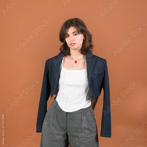 A square composition featuring a young brunette woman with a jacket draped over her shoulders, wearing a white corset, radiating confidence and style.