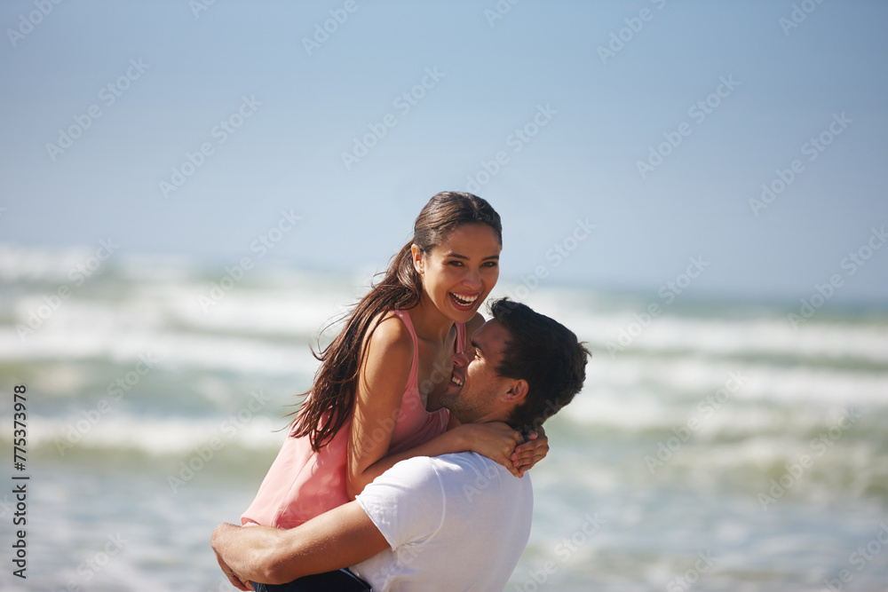 Happy couple, hug and beach with embrace for love, care or support on holiday, weekend or outdoor vacation. Man lifting woman with smile for relationship, summer fun or bonding by the ocean coast