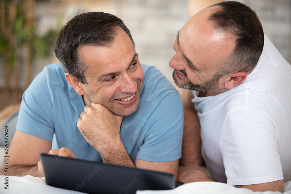 happy gay couple with tablet computer on bed at home happy gay couple with tablet computer on bed at home