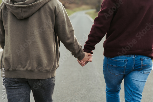 Close-up of anonymous couple holding hands, with a focus on their intertwined fingers, symbolizing love and connection on a quiet walk photo