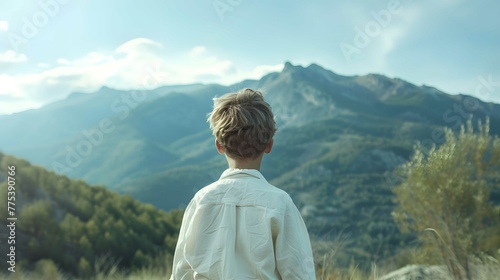 Young man sitting on top of a mountain and looking at the valley.