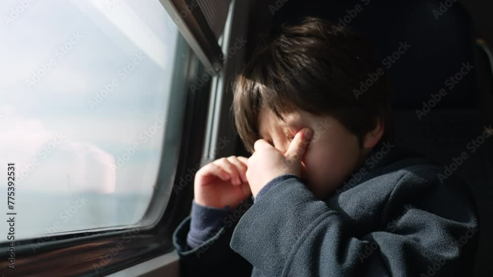 Tired young boy rubbing face and eyes while traveling by train. drowsy traveller child seated by window inside high-speed transportation Tired young boy rubbing face and eyes while traveling by train. drowsy traveller child seated by window inside high-speed transportation