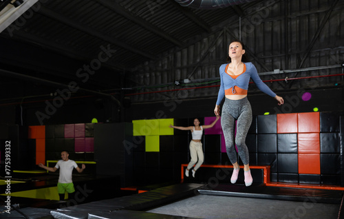 Happy middle-aged woman practicing and jumping on trampolines in a sports indoor center, workout and modern entertainment concept