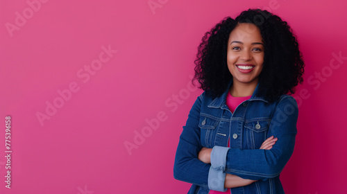 Mulher sorrindo de braços cruzados vestindo jeans azul no fundo rosa