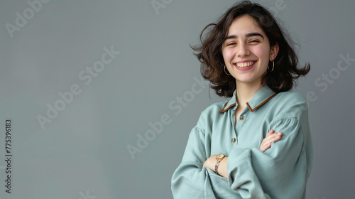 Mulher sorrindo de braços cruzados vestindo azul claro no fundo cinza