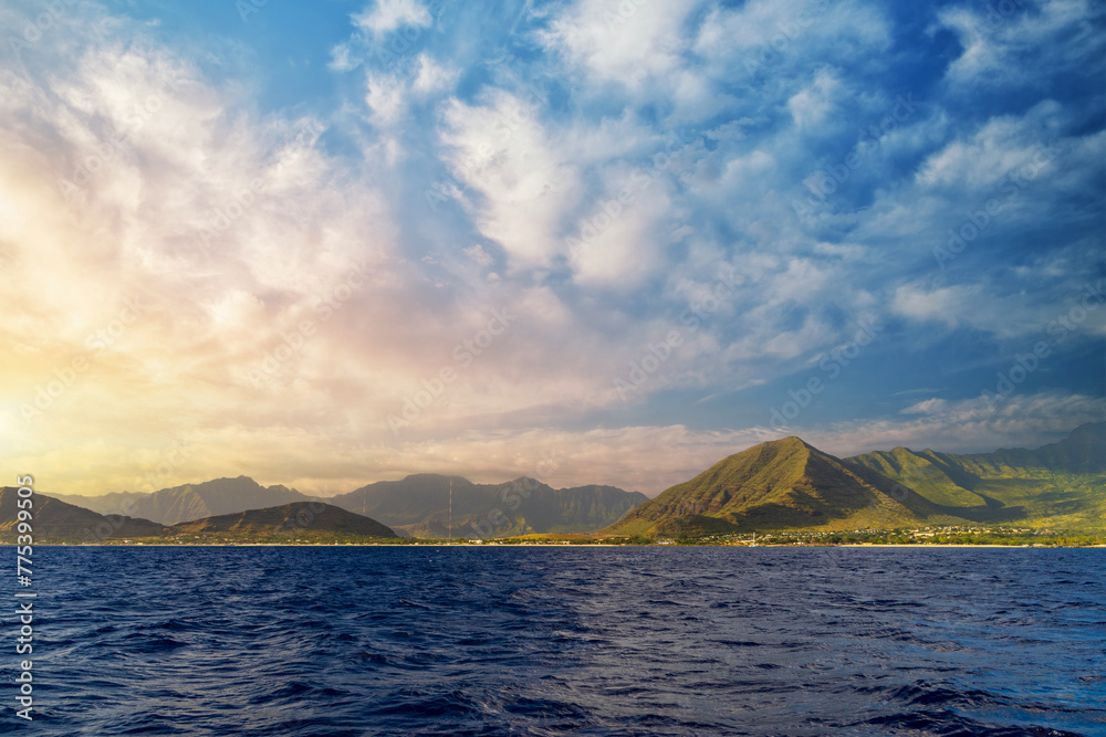 a beautiful spring landscape of the coast of Oahu with majestic mountain ranges, lush green trees and plants, rippling blue ocean water and blue sky with clouds at sunset in Kapolei Hawaii USA a beautiful spring landscape of the coast of Oahu with majestic mountain ranges, lush green trees and plants, rippling blue ocean water and blue sky with clouds at sunset in Kapolei Hawaii USA
