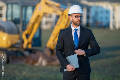 Architect at a construction site. Architect man in suit and helmet at construction site. Confident architect standing at construction. Investor or civil engineer. Outdoor portrait of hispanic