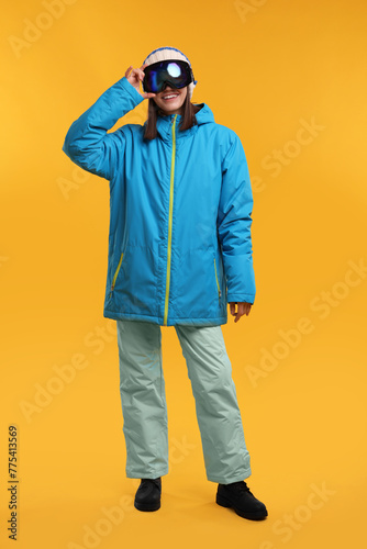 Winter sports. Happy woman with snowboard goggles on orange background