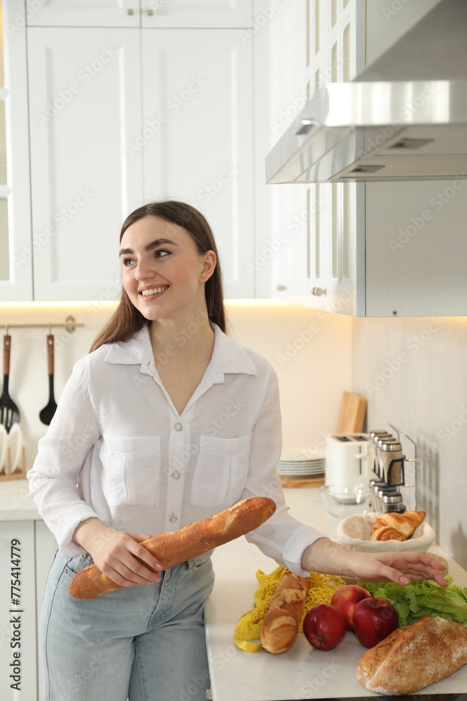 Woman with baguette and other products in kitchen