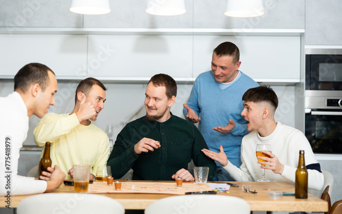 Cheerful young adults enjoying beer and wine immersed in board game with twist, where shot glasses of alcoholic drinks replacing traditional game pieces