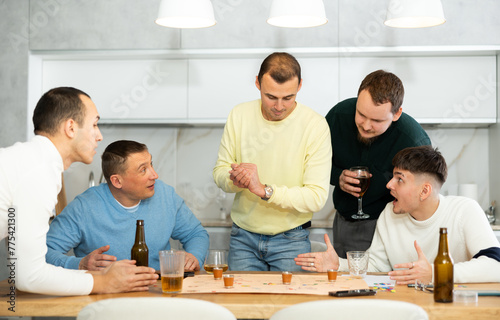 Group of adult friends excitedly playing board games and drinking beer at home