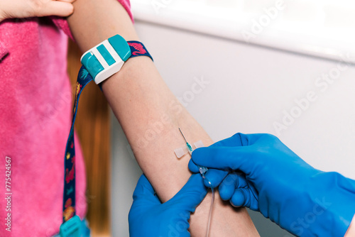 The image captures a moment during a blood sampling procedure where anonymous professional in blue gloves expertly inserts a butterfly needle into a patient's vein photo