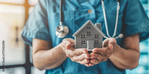 A nurse is holding a house in her hands. The house is made of metal and has a silver color. The nurse is wearing a blue uniform
