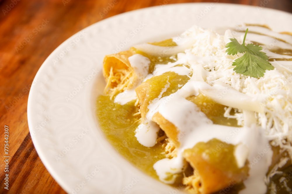Green enchiladas. Typical Mexican dish made with a folded or rolled corn tortilla filled with shredded chicken and covered with spicy green sauce, cream, grated cheese and onion. Green enchiladas. Typical Mexican dish made with a folded or rolled corn tortilla filled with shredded chicken and covered with spicy green sauce, cream, grated cheese and onion.
