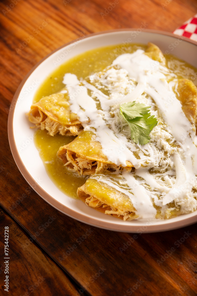 Green enchiladas. Typical Mexican dish made with a folded or rolled corn tortilla filled with shredded chicken and covered with spicy green sauce, cream, grated cheese and onion. Green enchiladas. Typical Mexican dish made with a folded or rolled corn tortilla filled with shredded chicken and covered with spicy green sauce, cream, grated cheese and onion.