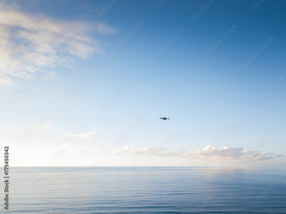 Seascape with a drone flying in the blue sky and clouds.