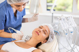 Young adult female patient experiencing cryotherapy procedure on neck using ice hammer to tighten skin in aesthetic medicine clinic. Advanced hardware cosmetology techniques