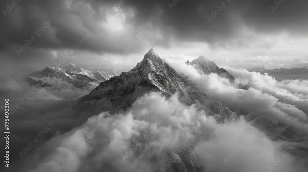 A black and white photograph of a solitary mountain peak surrounded by a sea of dark clouds with hints of fire peeking through. The aerial perspective highlights the isolation