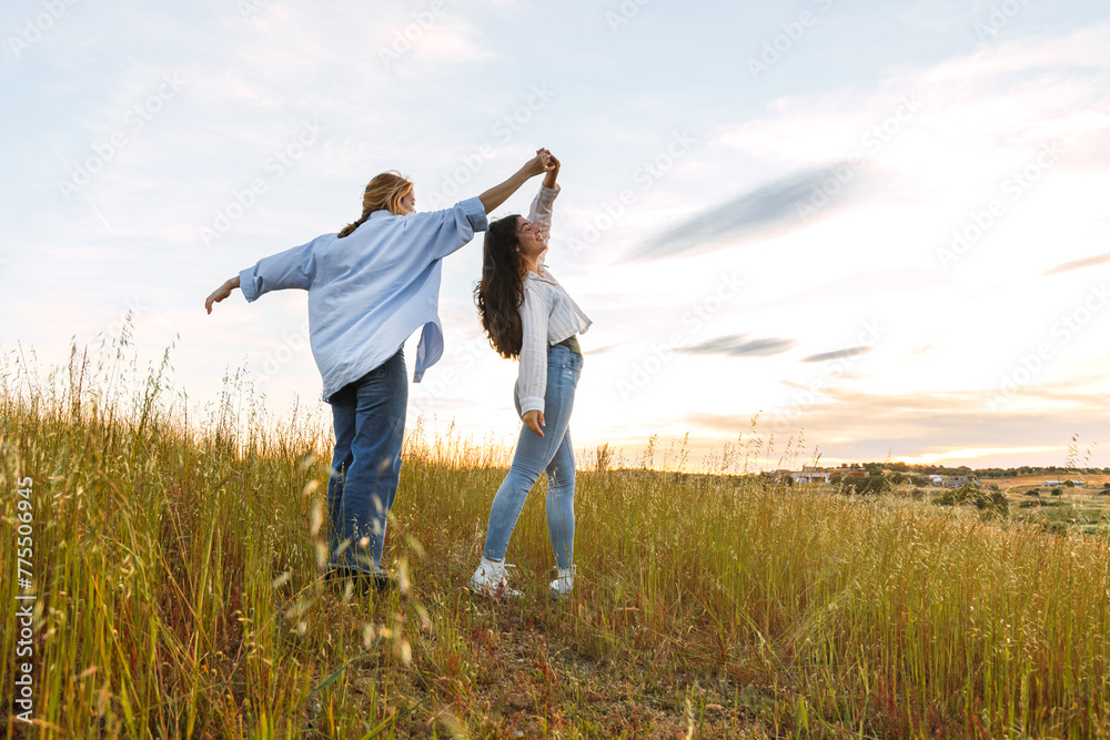 two women friends having fun in a field at sunset