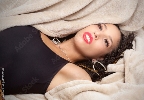 Glamorous young Latina woman reclining into a tan blanket.