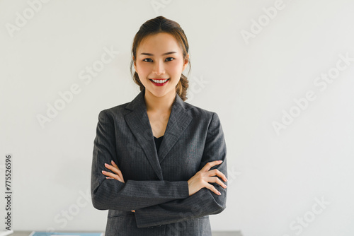 Professional Asian businesswoman smiling confidently with her arms crossed, wearing a grey suit in office. photo